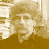 Liberto Cruz: Retrato de um homem com cabelos crespos e volumosos, bigode e óculos, em tons de sépia, com uma estante de livros ao fundo.