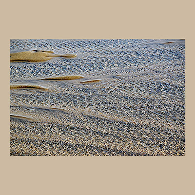 unknown: Uma fotografia detalhada de água rasa fluindo sobre areia e seixos de uma praia, criando padrões texturizados.