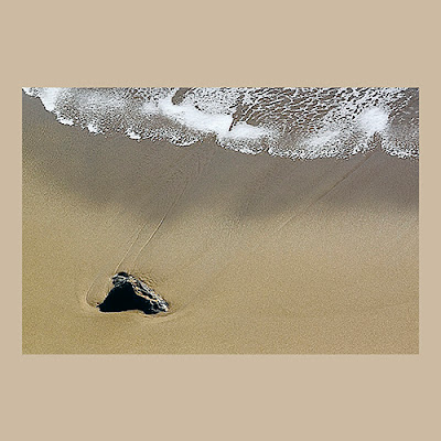 unknown: Uma fotografia artística de uma pequena rocha na areia de uma praia, com a espuma de uma onda se aproximando.
