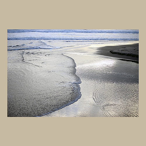 Uma fotografia artística de ondas suaves quebrando na areia de uma praia com reflexos de luz.