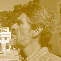 Retrato de perfil em tom sépia de um homem com barba e cabelo grisalho, vestindo uma camisa xadrez.