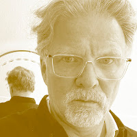 Luís Carmelo: Retrato em tom sépia de um homem de óculos e barba grisalha, com seu reflexo visível ao fundo.