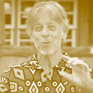 António Manuel Ribeiro: Retrato em tom sépia de um homem falando, vestindo uma camisa com estampas geométricas.