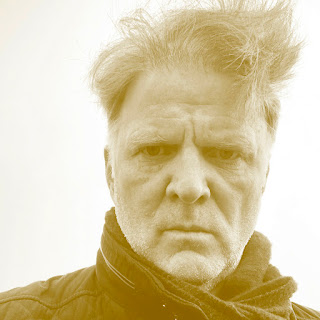 Valter Hugo Mãe: Retrato em close-up de um homem com expressão séria, cabelos grisalhos desalinhados e usando um cachecol, com filtro em tons de sépia amarelado.