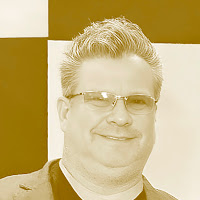 Retrato em tons sépia de um homem sorrindo, usando óculos.