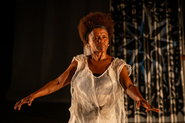 Rosana Paulino: Uma mulher negra de cabelos crespos usando uma roupa branca texturizada em uma performance teatral ou de dança.