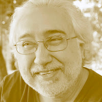 António Pelarigo: Retrato em tom sépia de um homem mais velho sorrindo, com cabelos brancos, barba e óculos.