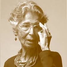 Maria Gabriela Llansol: Retrato de uma mulher idosa com óculos, usando um colar e brincos, ajustando os óculos com a mão esquerda.