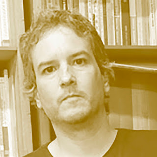 Jeferson Tenório: Retrato em tom sépia de um homem com cabelos ondulados em frente a uma estante de livros.