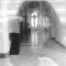 Fotografia de baixa resolução em preto e branco mostrando o interior de uma estrutura de pedra, possivelmente uma igreja ou capela, com uma abertura em formato de cruz ao fundo.
