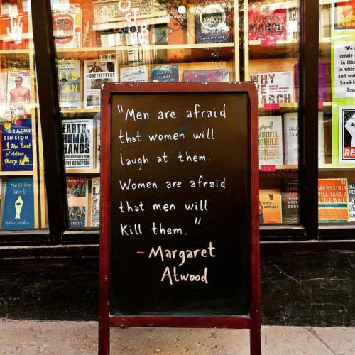 Margaret Atwood: Uma lousa de calçada em frente a uma livraria com uma citação de Margaret Atwood escrita à mão.