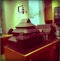 Maquete de uma estrutura arquitetônica tradicional de madeira, possivelmente uma igreja ou templo, exposta em um ambiente de museu ou galeria.