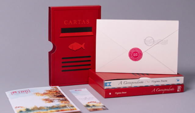 Conjunto de itens literários da TAG Experiências Literárias, incluindo o livro 'A Correspondente' de Virgínia Reeves, um envelope e uma caixa temática que imita uma caixa de correio.