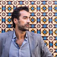 António Casalinho: Retrato de um homem de barba e blazer encostado em uma parede de azulejos portugueses.