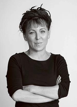 Olga Tokarczuk: Retrato em preto e branco de uma mulher com os braços cruzados e dreadlocks presos no topo da cabeça.