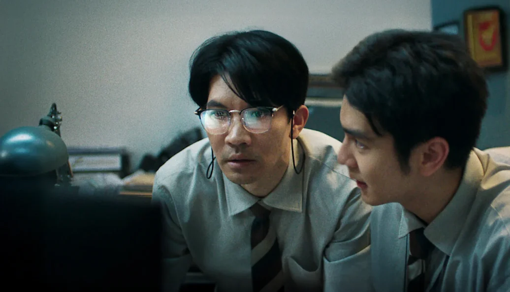 desconhecido: Cena de filme mostrando dois homens com roupas de escritório olhando atentamente para a tela de um computador.