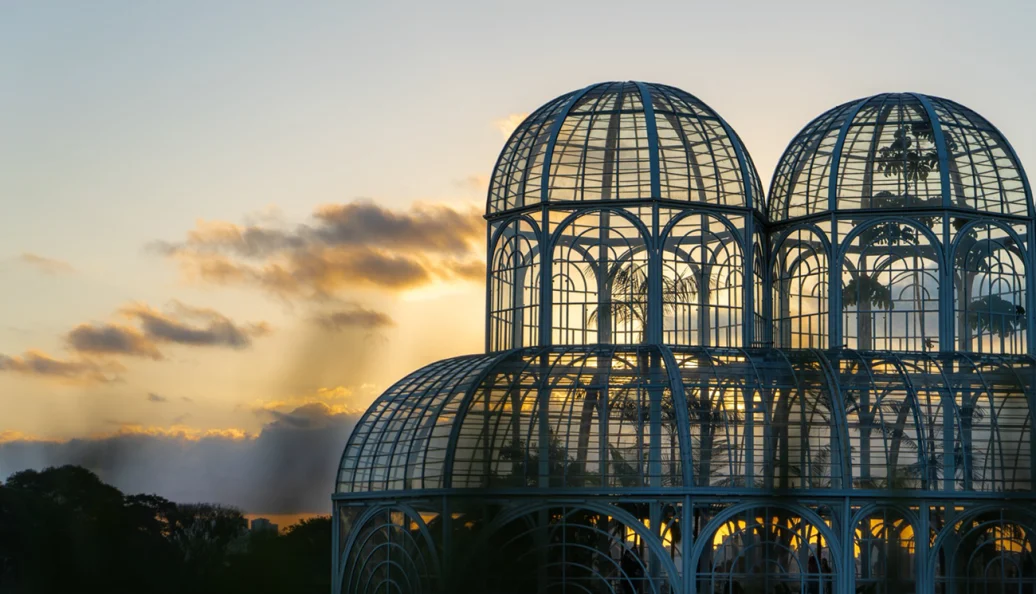 Estufa de vidro e metal do Jardim Botânico de Curitiba ao entardecer.