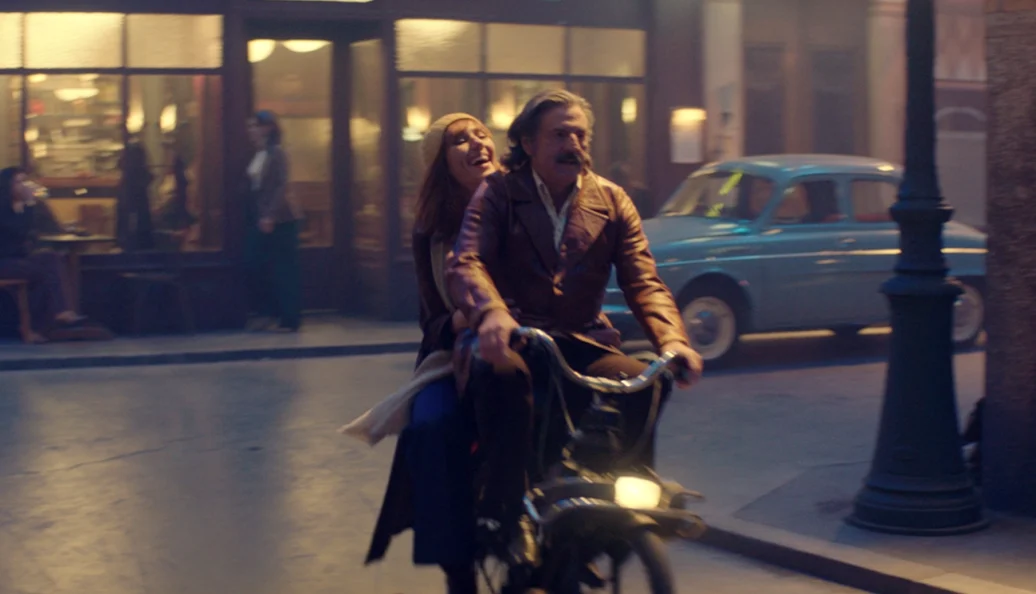 Daniel Auteuil, Fanny Ardant: Uma cena do filme 'La Belle Époque' mostrando um homem e uma mulher andando de bicicleta em uma rua cenográfica noturna.