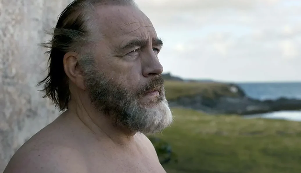 Brian Cox: Close-up profile of an older man with a gray beard outdoors near the sea.