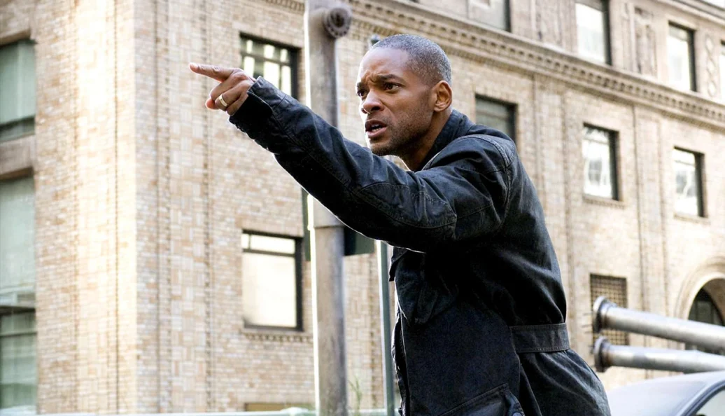 Will Smith: Cena do filme 'Eu Sou a Lenda' mostrando o protagonista apontando para frente com expressão séria em um cenário urbano.