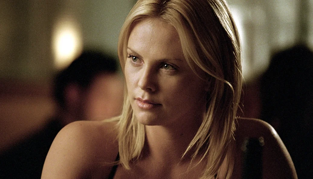 Charlize Theron: Close-up de uma mulher loira em um ambiente de iluminação suave, cena do filme The Italian Job.