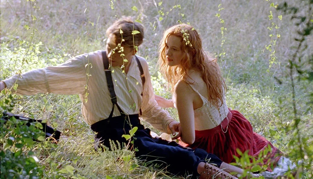 Sam Neill, Holly Hunter: Cena do filme O Piano, mostrando os personagens Stewart e Ada sentados na grama em uma área arborizada.