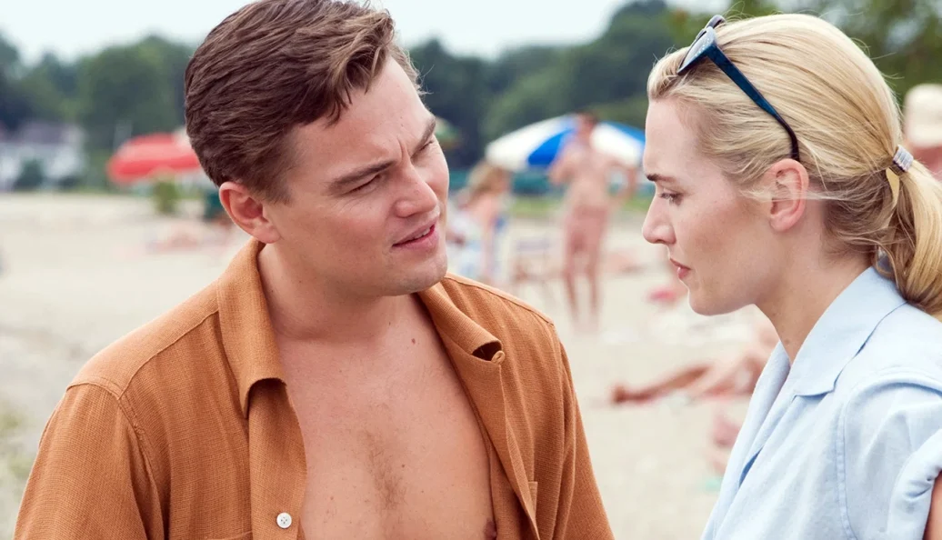 Leonardo DiCaprio, Kate Winslet: Uma fotografia de cena de filme mostrando Leonardo DiCaprio e Kate Winslet conversando em uma praia.