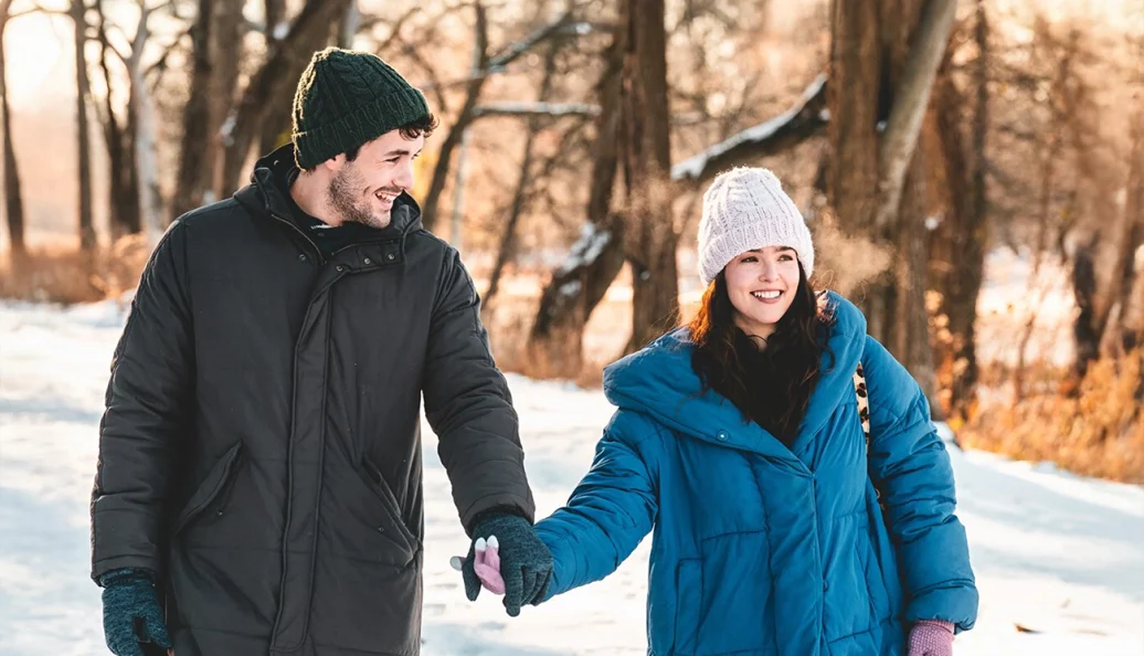 Zoey Deutch: Um casal caminhando e sorrindo de mãos dadas em um cenário de inverno com neve.