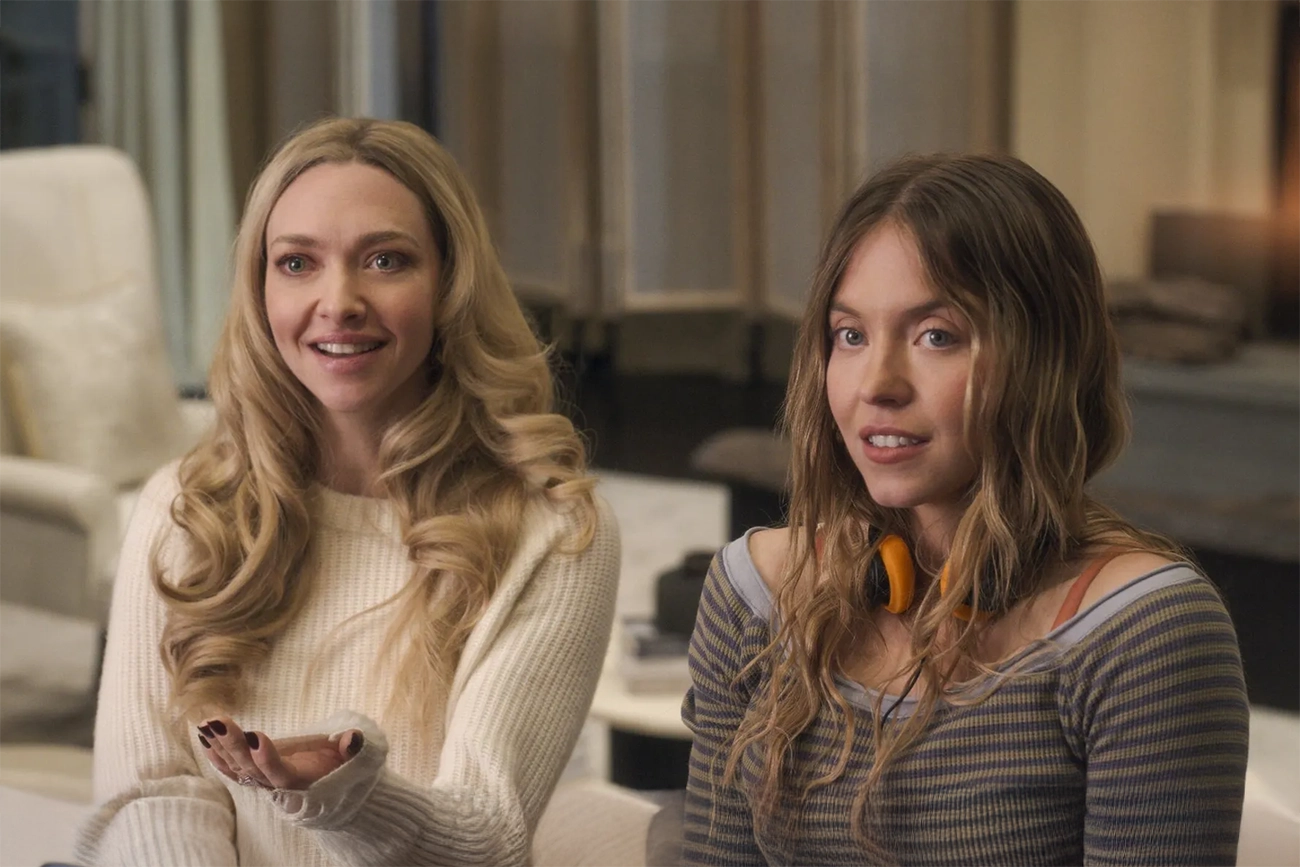 Amanda Seyfried, Sydney Sweeney: Duas mulheres sorrindo em um ambiente interno, possivelmente uma cena de filme.