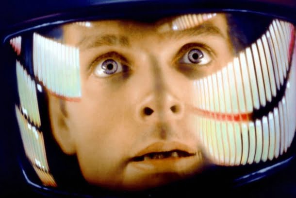 Keir Dullea: Close-up do rosto de um astronauta dentro de um capacete com reflexos de luzes, cena do filme 2001: Uma Odisseia no Espaço.