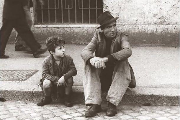Lamberto Maggiorani, Enzo Staiola: Cena em preto e branco do filme Ladrões de Bicicleta (1948), mostrando um homem e um menino sentados na calçada.