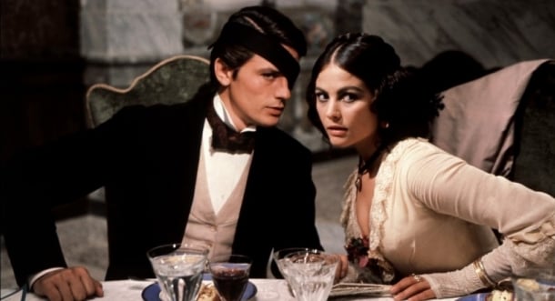 Alain Delon, Claudia Cardinale: Cena do filme O Leopardo (Il Gattopardo), mostrando um homem com tapa-olho e uma mulher em trajes de época sentados à mesa.