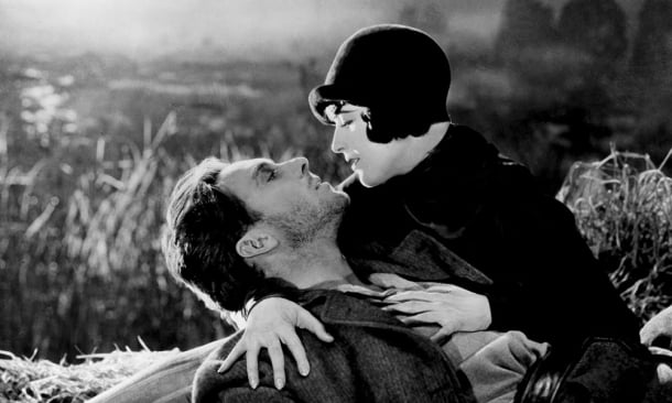 George O'Brien e Margaret Livingston: Cena em preto e branco do filme Sunrise: A Song of Two Humans (1927), mostrando um homem deitado e uma mulher inclinada sobre ele em um campo.