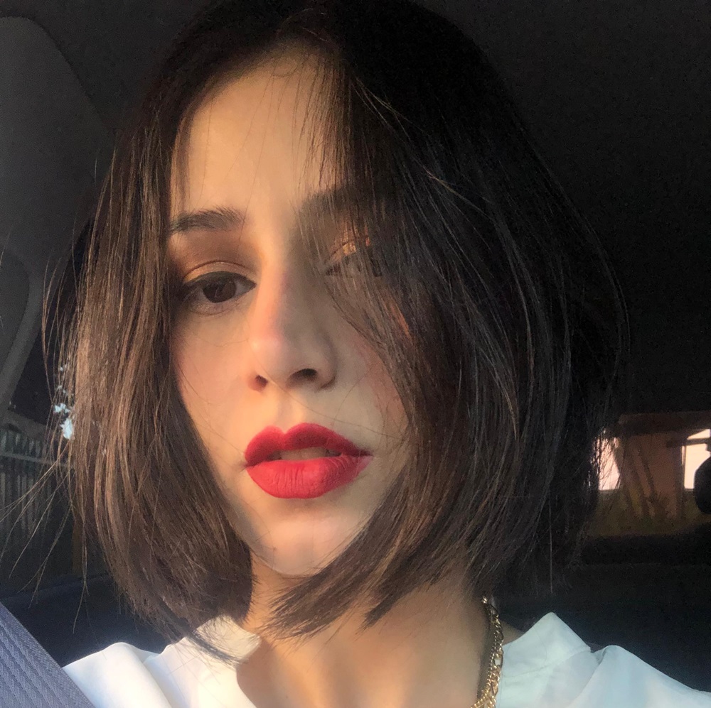 desconhecido: Selfie de uma mulher com cabelo curto escuro e batom vermelho, tirada dentro de um carro.