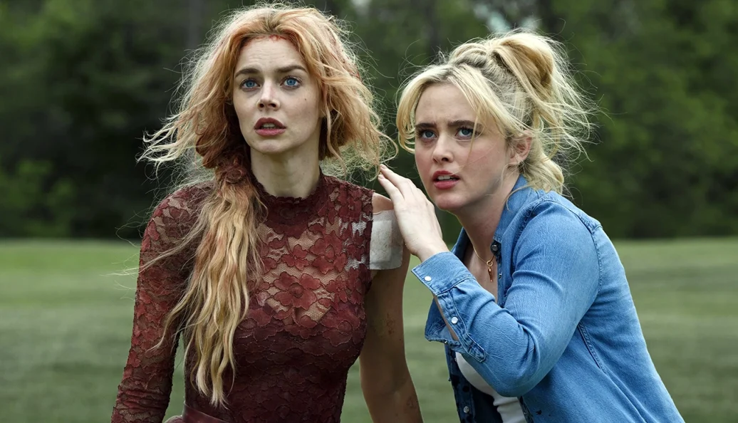 Samara Weaving, Kathryn Newton: Duas mulheres com expressões de preocupação e choque em um campo gramado, cena do filme Lisa Frankenstein.