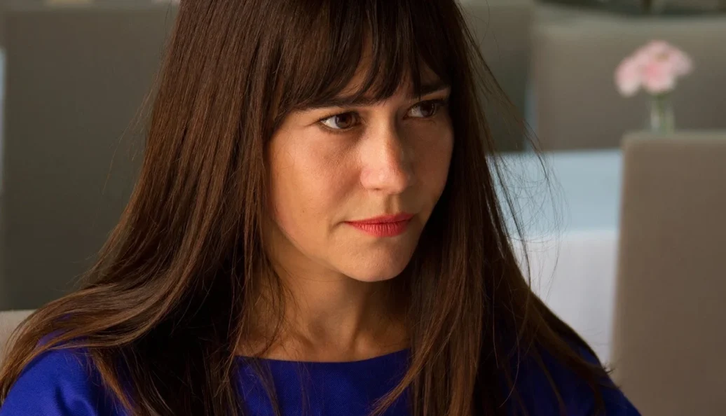 Alessandra Negrini: Close-up de uma mulher de cabelos castanhos com franja, vestindo uma blusa azul, com olhar sério ou reflexivo.