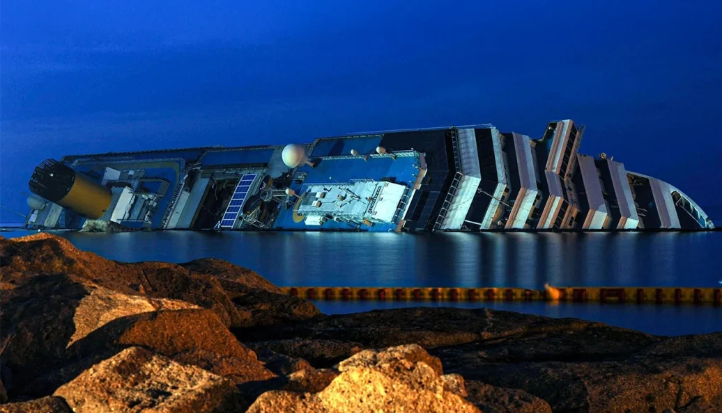 O navio de cruzeiro Costa Concordia naufragado e tombado de lado na costa da Ilha de Giglio, Itália, iluminado à noite.