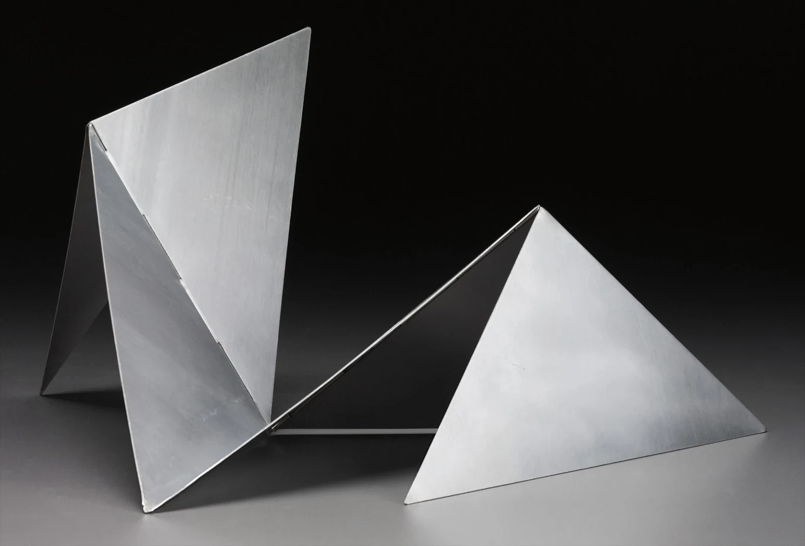 Lygia Clark: Uma fotografia de estúdio de uma escultura neoconcreta feita de placas de metal angulares e dobradas, com iluminação dramática contra um fundo escuro.