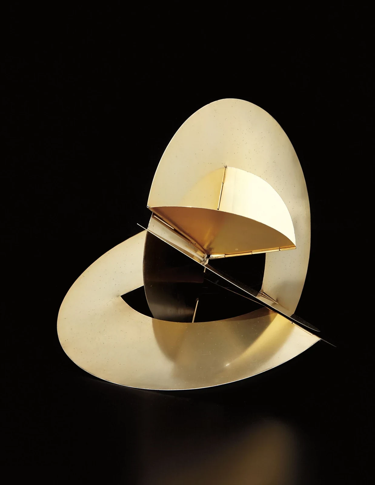 Lygia Clark: Uma escultura geométrica e abstrata de metal dourado composta por planos circulares e angulares sobre um fundo preto.