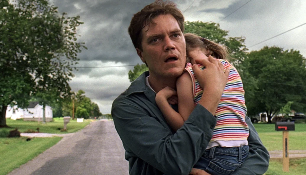 Michael Shannon: Cena do filme Take Shelter mostrando um homem segurando uma criança sob um céu de tempestade.