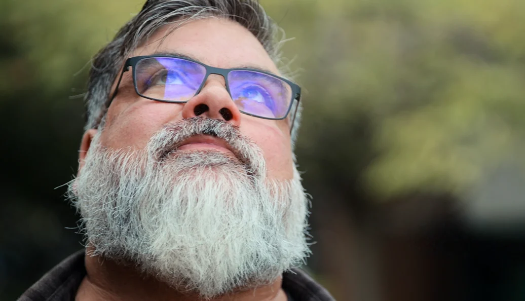 J.P. Cuenca: Retrato em close-up de um homem com barba grisalha e óculos olhando para cima.