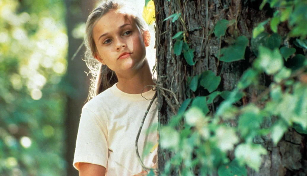 Reese Witherspoon: Uma jovem Reese Witherspoon encostada em uma árvore em um ambiente de floresta, cena do filme The Man in the Moon.