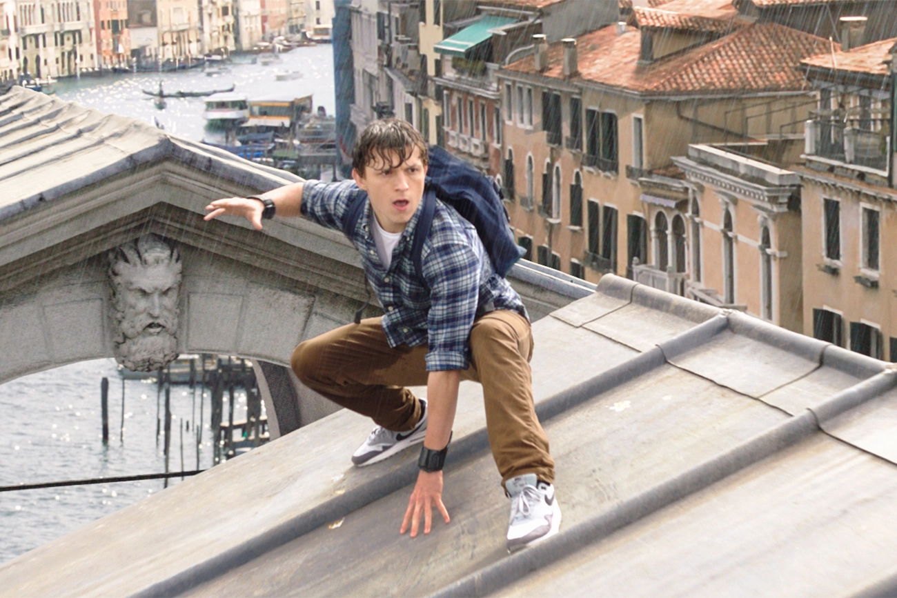 Tom Holland: Cena do filme Homem-Aranha: Longe de Casa, mostrando Peter Parker agachado em um telhado em Veneza sob a chuva.