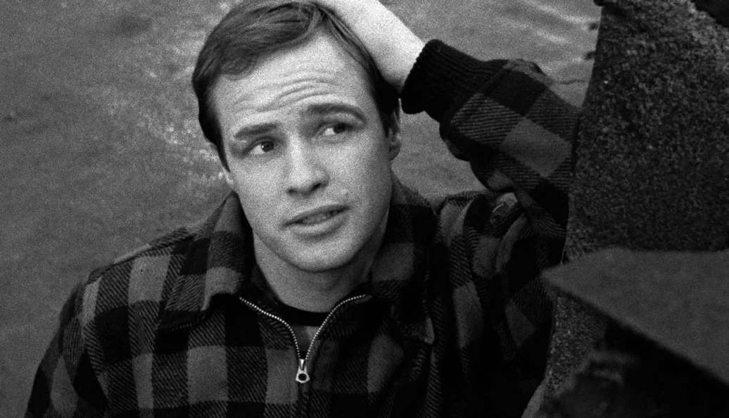 Marlon Brando: Retrato em preto e branco de Marlon Brando no filme 'Sindicato de Ladrões' (On the Waterfront), vestindo uma jaqueta xadrez.