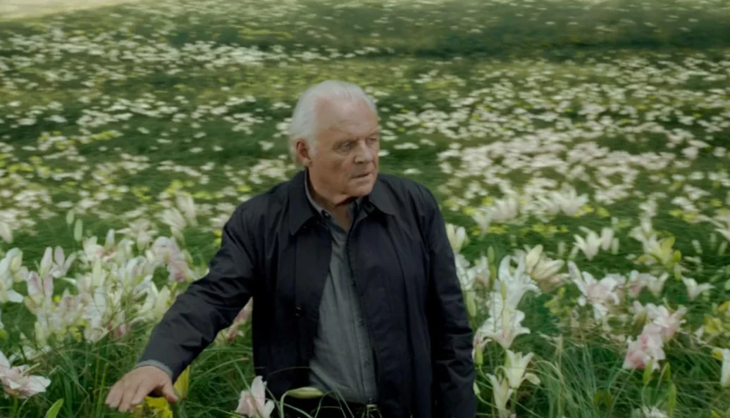 Anthony Hopkins: Cena da série Westworld onde o personagem Dr. Robert Ford caminha por um campo de flores brancas.
