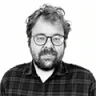 João Tordo: Retrato em preto e branco de um homem com barba, óculos e camisa xadrez.