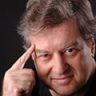 Stephen Fry: Retrato em close-up de um homem de meia-idade apontando o dedo indicador para a têmpora em um gesto de pensamento ou ideia.