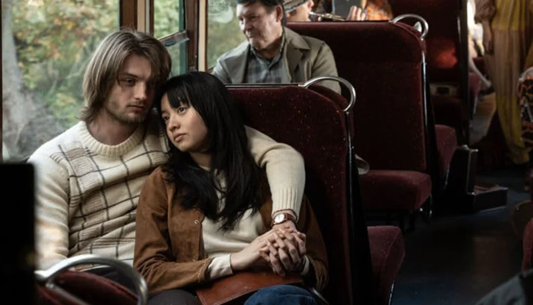 Alex Neustaedter, Mizuki Tsujimura: Uma cena de filme mostrando um jovem casal abraçado em um banco de trem ou ônibus.