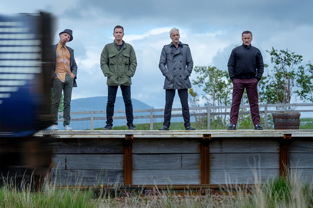 Ewen Bremner, Ewan McGregor, Jonny Lee Miller, Robert Carlyle: Quatro homens em pé em uma plataforma de trem rural, cena do filme T2 Trainspotting.