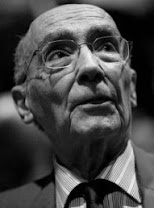 José Saramago: Retrato em close-up de um homem idoso usando óculos, olhando ligeiramente para cima.